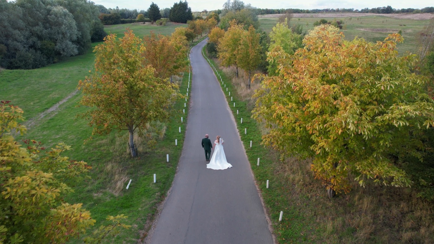 Aerial shot of a bride on a lane through autumn trees
