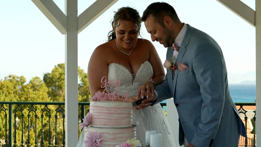 A couple cutting their cake on a seaside terrace