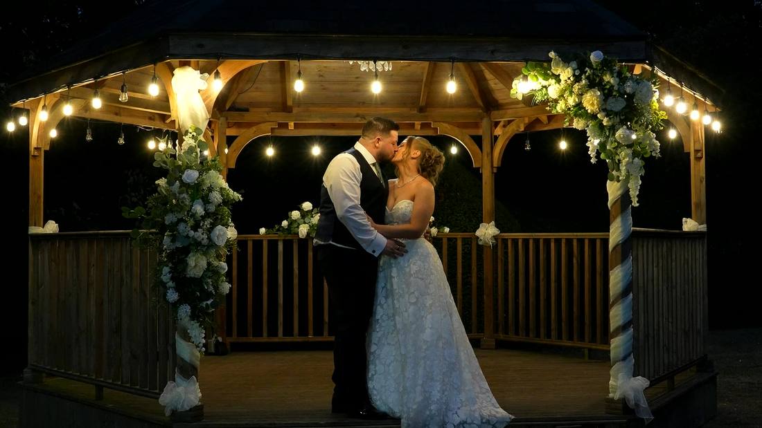 A couple kissing in a lit gazebo at night