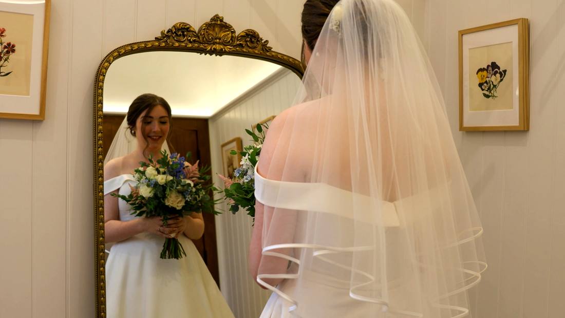 A bride in her veil looking at herself in a gilded mirror